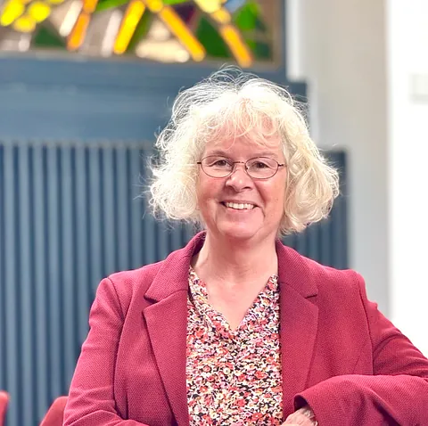 Lächelnde Frau mit Brille und weißen lockigen Haaren in einer Kirche.